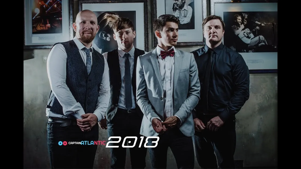 Four men dressed in formal attire standing in front of black and white framed photos on a wall, with text 'Captain Atlantic 2018'.