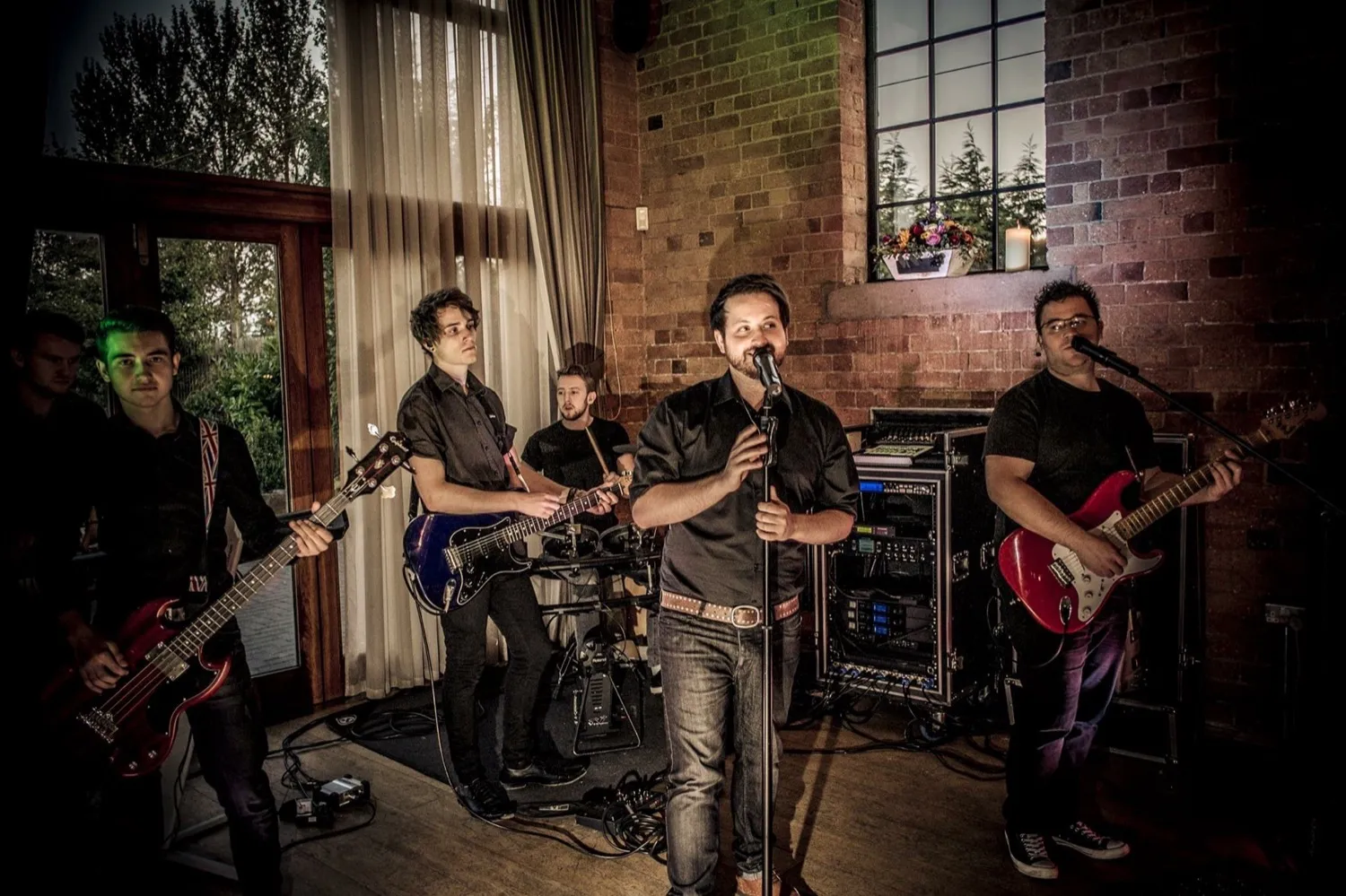 Five-member band performing indoors with two guitarists, a bassist, a drummer, and a singer at the microphone.