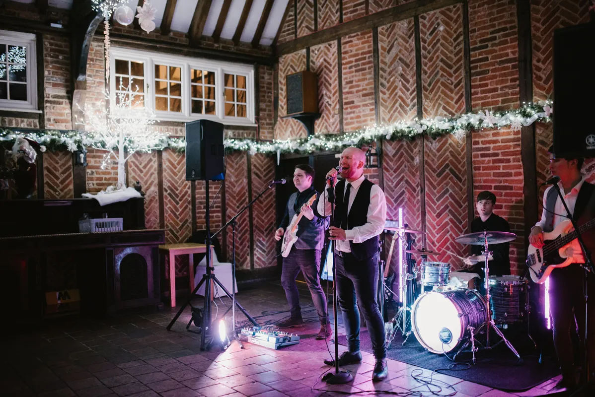 Four-piece band performing indoors with brick walls decorated with garlands and fairy lights.