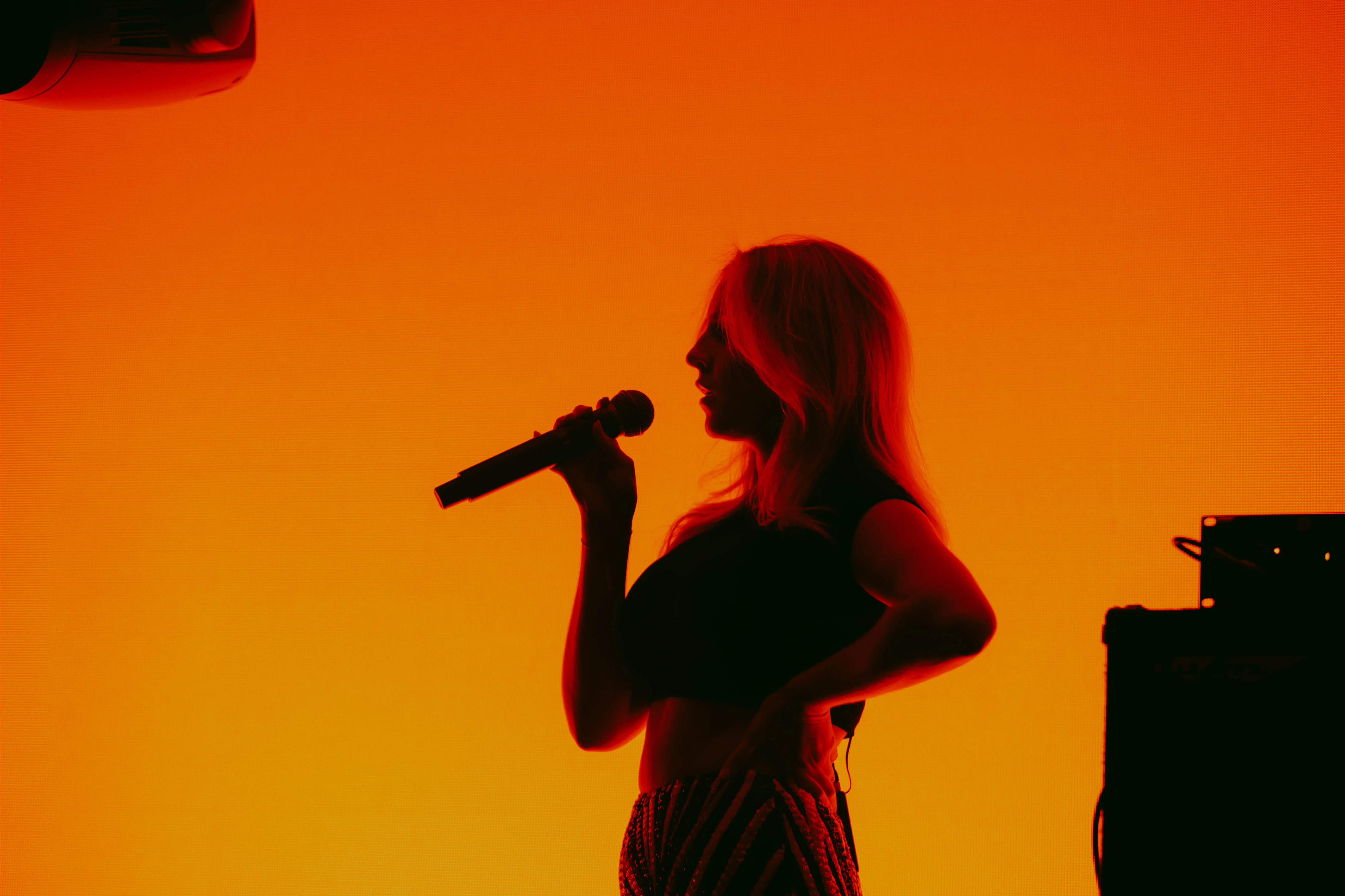Silhouette of a woman holding a microphone against a vibrant orange background.