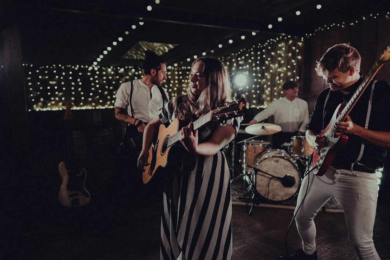 Four-piece band playing instruments with string lights and fairy lights in the background.